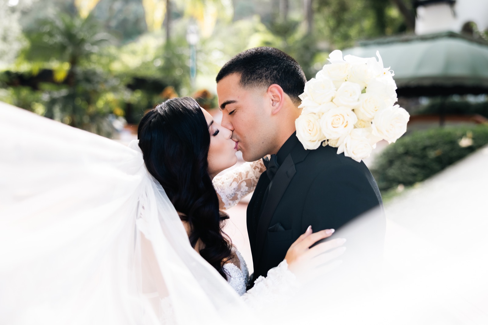 Mikey and Michelle kissing with veil flowing and white roses at Rancho Las Lomas