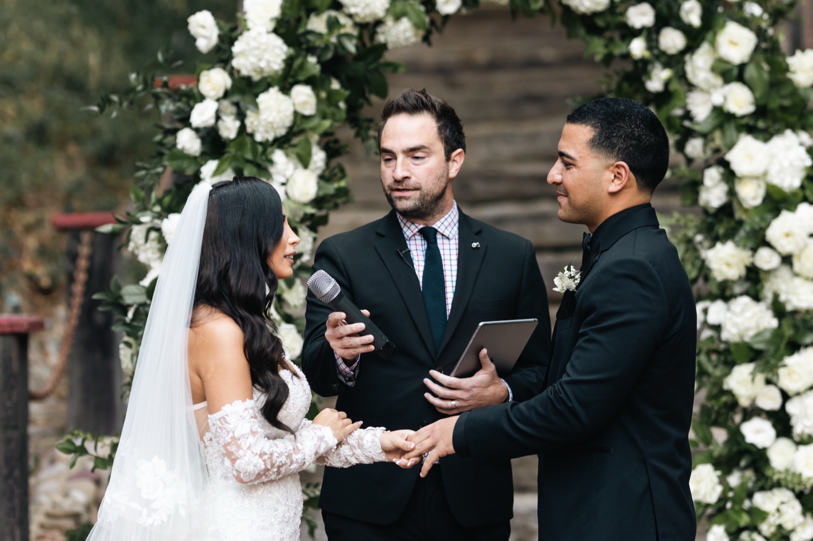 Mikey and Michelle exchanging vows with officiant under floral arch at Rancho Las Lomas