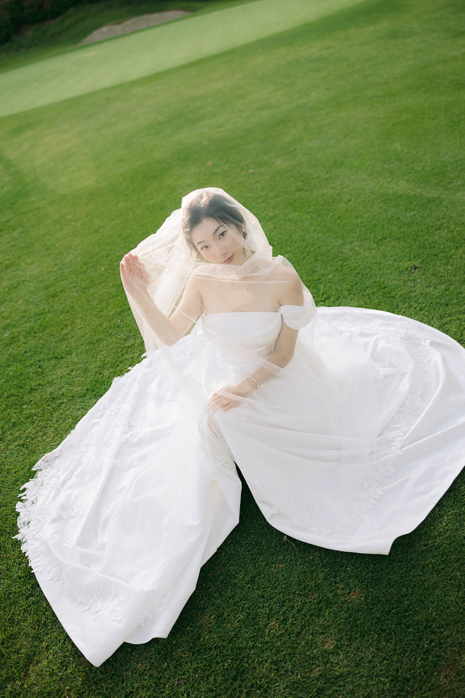 Bride sitting on golf course with veil in the wind