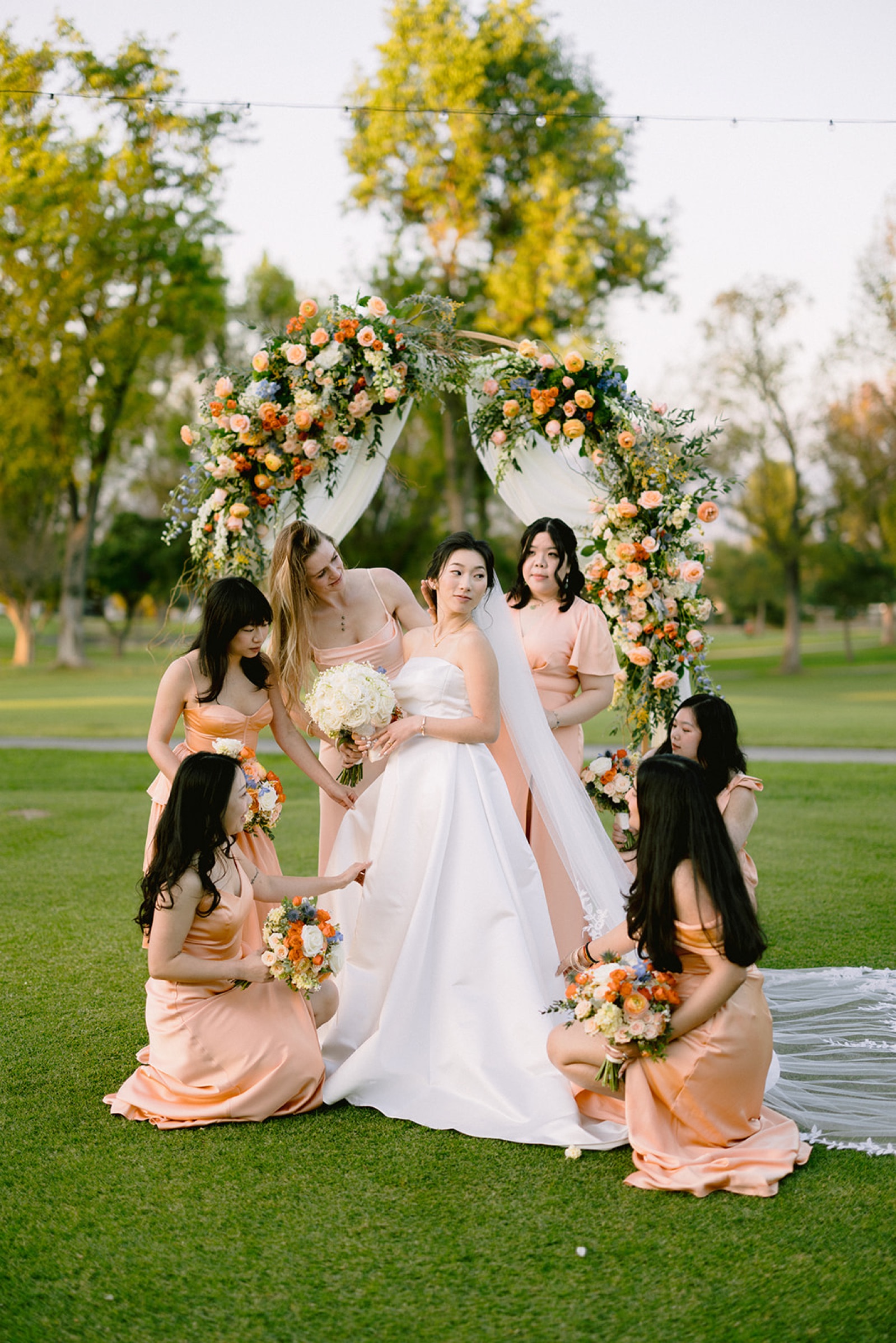 Bride with bridesmaids in peach dresses under the floral arch