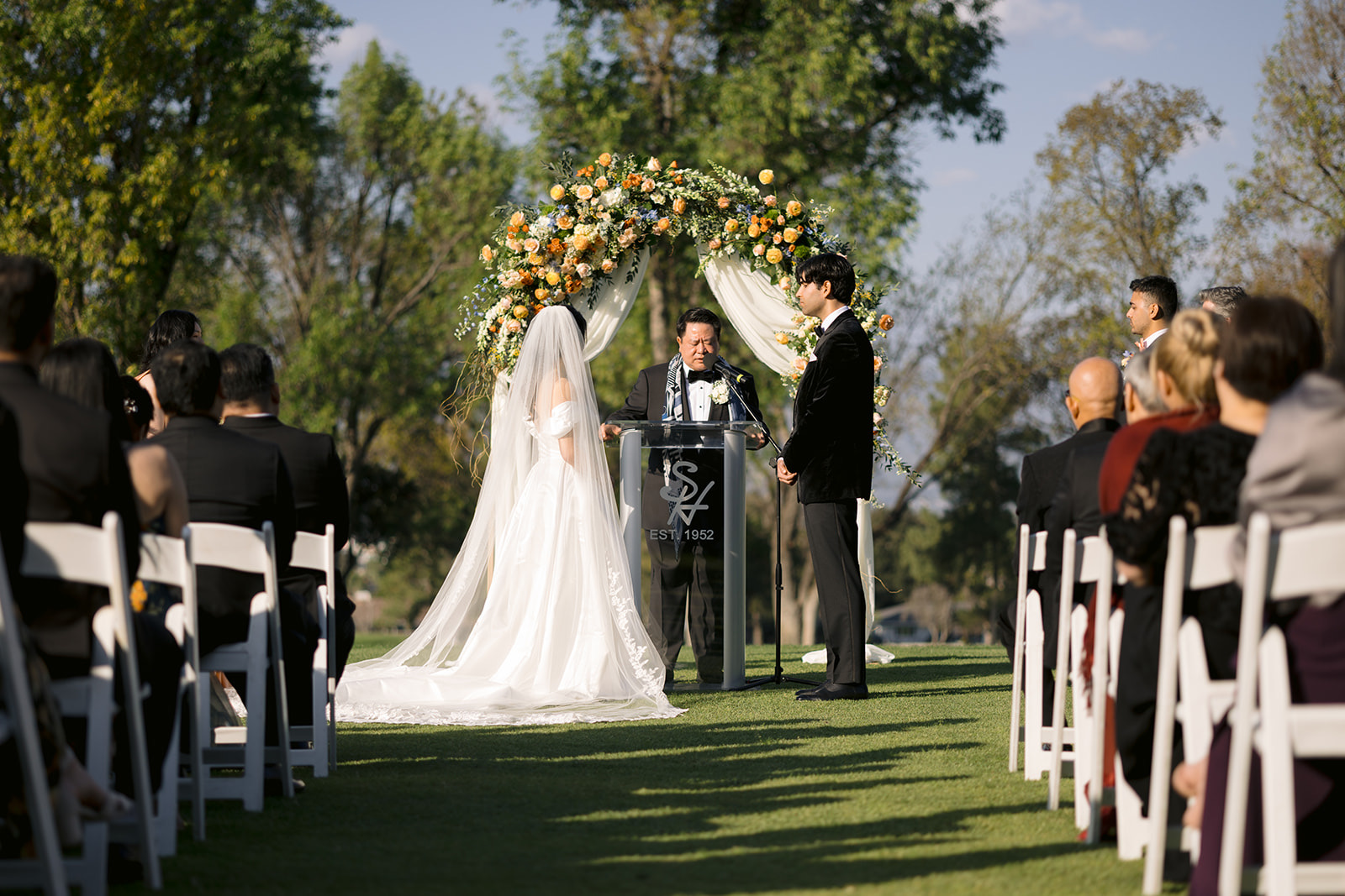Wide shot of the ceremony at South Hills Country Club with floral arch